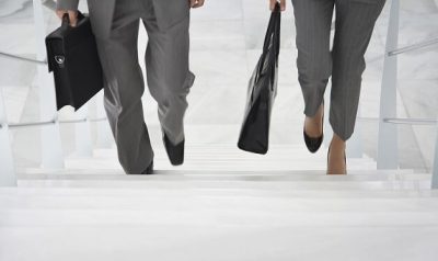 Bild für den Entwicklungs- und Karrierecoach. Mann und Frau in Businessoutfit laufen eine Treppe hoch. Nur die Füße und Taschen sind zu sehen.